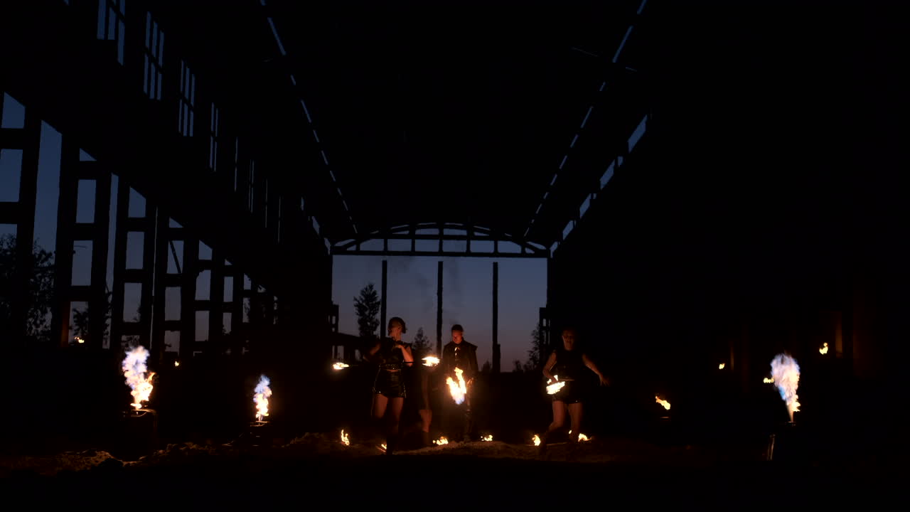 가죽 옷을 입은 네 명의 여성이 불 춤을 추고 불을 보여줍니다. 뒷면에 불꽃을 던지는 불꽃을 가진 남자가 느린 동작으로 불꽃을 가지고 놀고 있습니다.