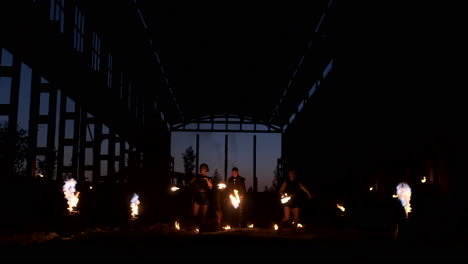 four women in leather clothes with fire dance and show fire show a man with a flamethrower in the back plays with the flame in slow motion