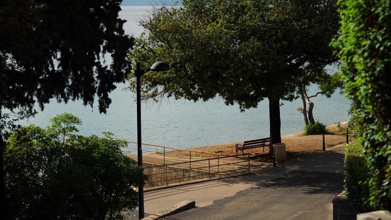 Calçadão tranquilo à beira-mar com banco, árvores e águas calmas do Adriático ao longo da costa croata durante um dia ensolarado