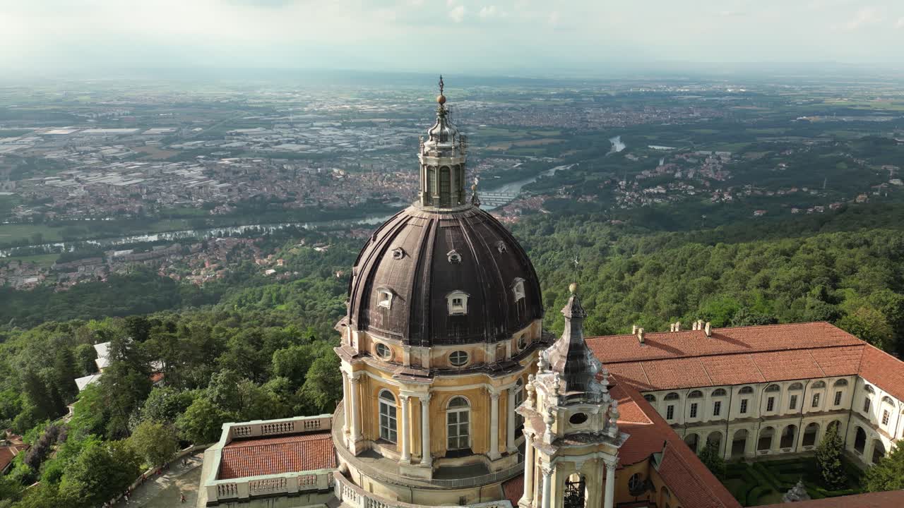 Orbita aerea con drone che rivela la grande cupola barocca della Basilica di Superga sopra il suo complesso monastico con tetti in terracotta, circondato da colline boscose vicino a Torino.