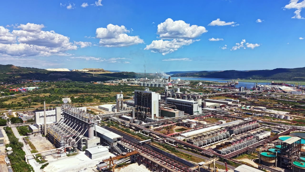 Complejo industrial con fábricas y productos contra un cielo azul en una región con colinas y un río