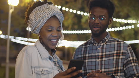 Afroamerikanische-Freunde-Nutzen-Smartphone-Und-Chatten-Abends-Im-Freien