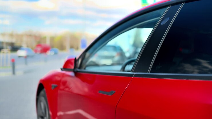 Primo piano di una donna che apre la sua auto elettrica rossa con una tessera e sale a bordo