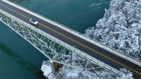 Vista-Aérea-De-Los-Automóviles-Que-Cruzan-Un-Puente-Con-Nieve-Que-Cubre-La-Tierra