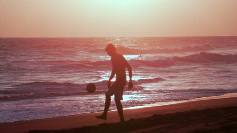 Silueta-De-Un-Joven-Jugando-Con-Una-Pelota-De-Fútbol-En-Sany-Beat-Al-Atardecer,-Cámara-Lenta