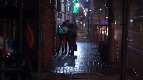 People-wait-outside-of-bar-as-woman-walks-by-holding-umbrella-under-snow-fall