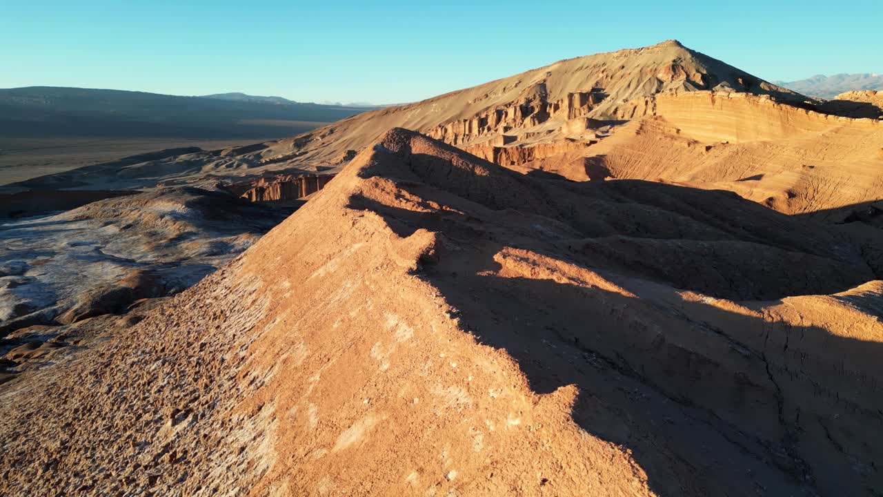 Drone aerial capturing the surreal desert of Valle de la Luna, with orange mountains glowing and salt flats shining at golden hour
