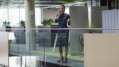 caucasian businesswoman talking on smartphone in corridor in modern office