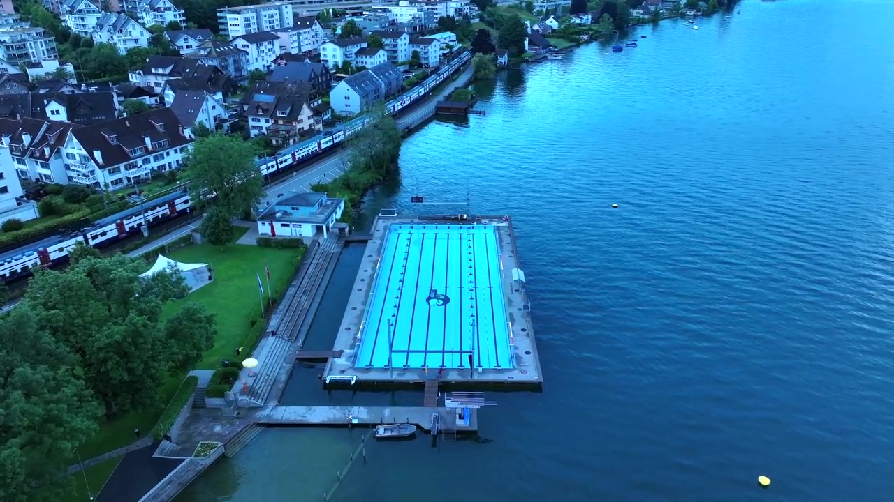 魅力的なスイスの町の湖畔に建てられたオリンピック様式のプールを旋回する空撮。