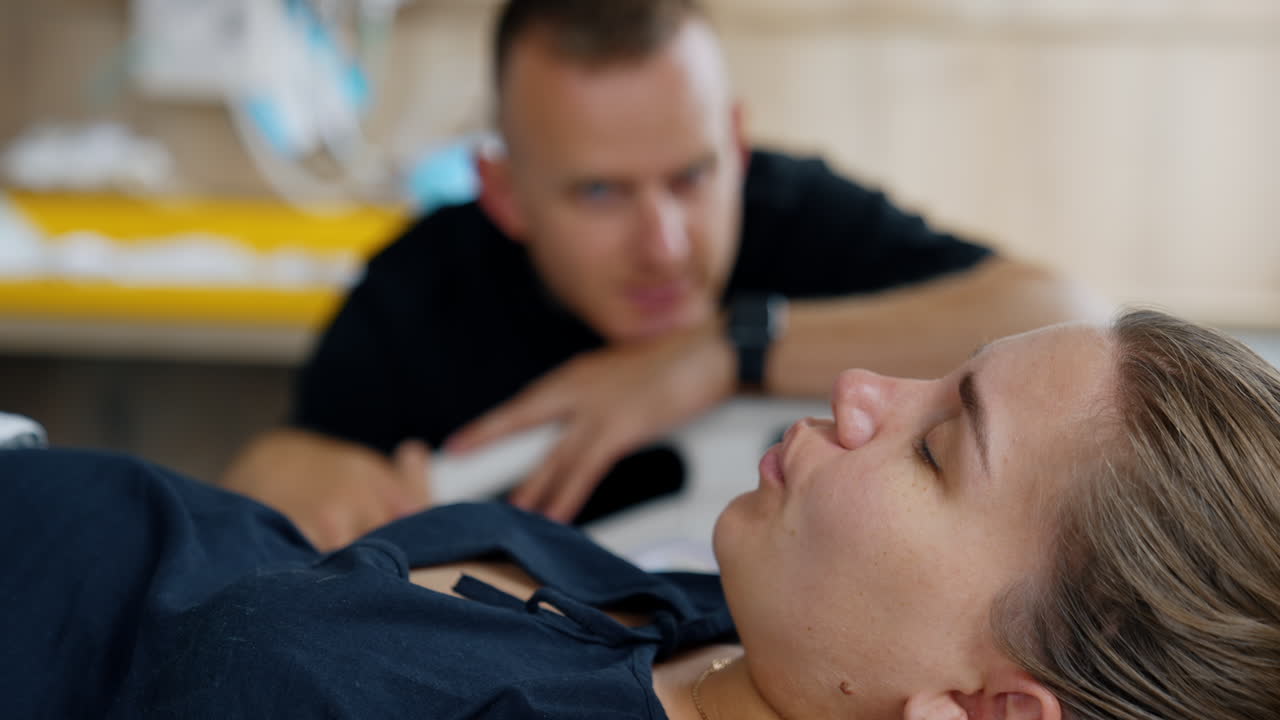 Caucasian woman is in process of childbirth. Future mom breathing slow with eyes closed. Man watching her at backdrop in blur.