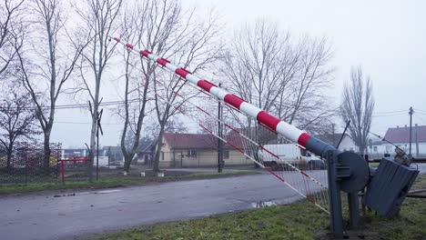 a red-and-white striped railway crossing barrier is raised, showing a small rural town in the background
