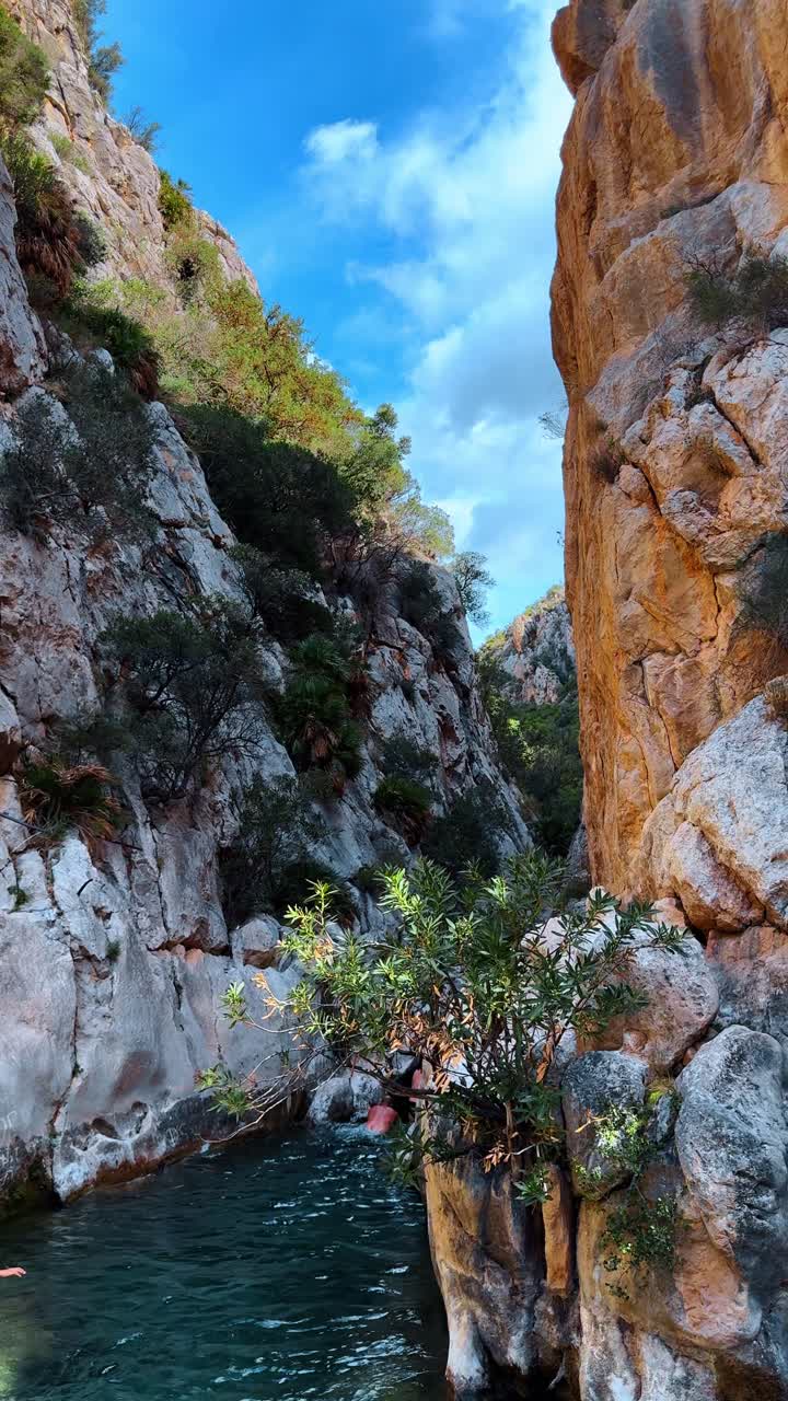 Stretto canyon con acque turchesi del fiume e ripide pareti rocciose. Vista dal livello dell'acqua di una gola rocciosa con un ruscello cristallino e vegetazione verde sulle pareti calcaree.
