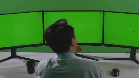 vista trasera de un hombre asiático cansado bostezando antes de dormir mientras trabaja con un simulacro de múltiples monitores de computadora en un estudio de pantalla verde