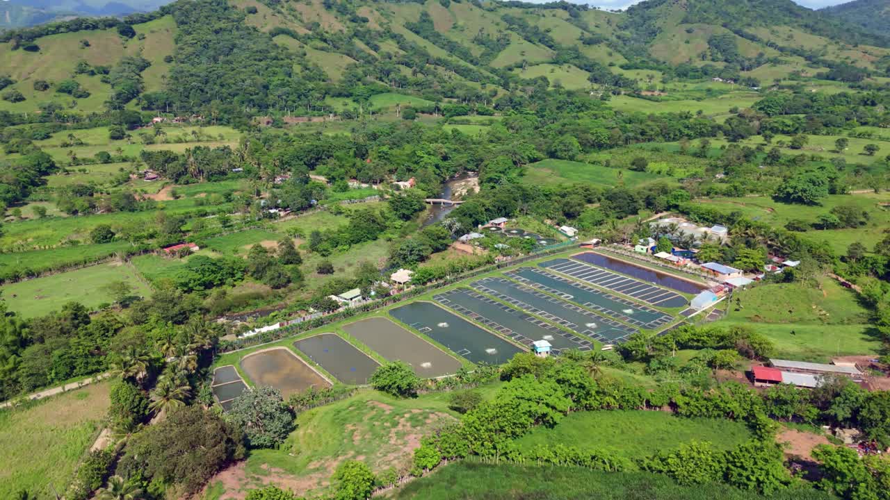 Series of rectangular aquaculture pond for fish farming, nestled in vibrant green valley with hills. Aerial drone orbiting