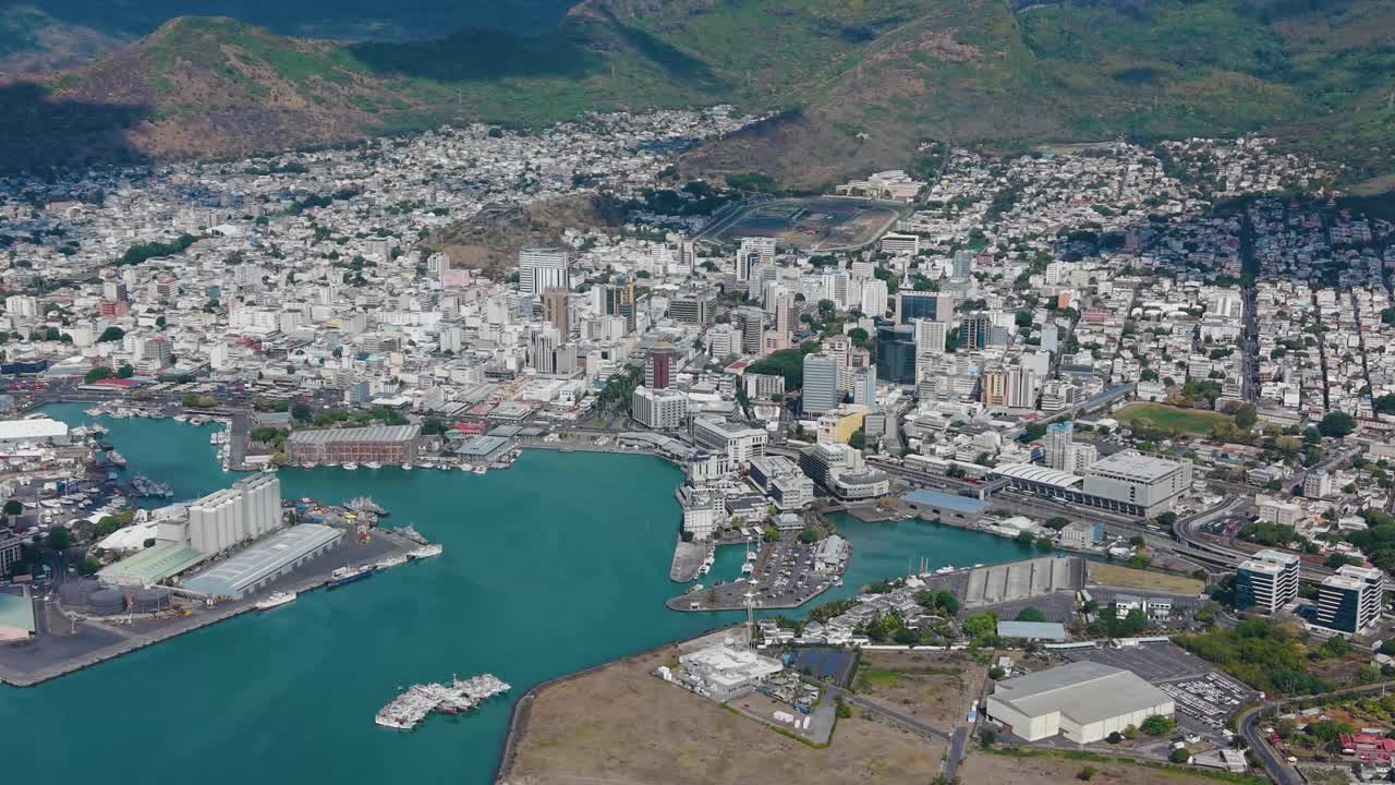 Aerial of the Port Louis skyline in Mauritius. Features the bustling Caudan Waterfront, with the city nestled against the Moka Mountains and the blue ocean
