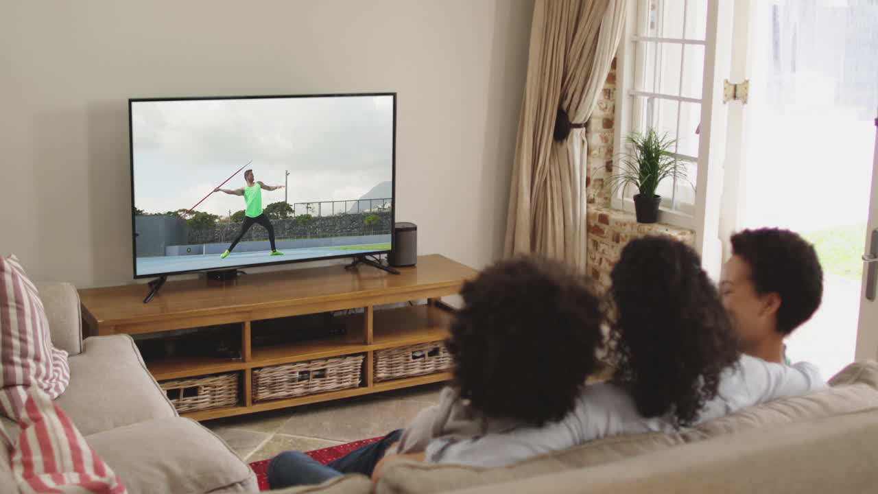 Composizione di famiglia felice seduta insieme a casa che guarda un evento di atletica leggera di lancio del giavellotto in TV.