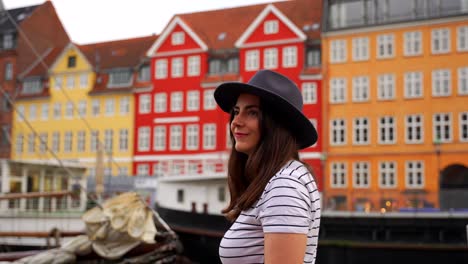 Mujer-Con-Sombrero-Y-Sonriendo-En-Nyhavn-Con-Casas-Coloridas-En-Segundo-Plano.