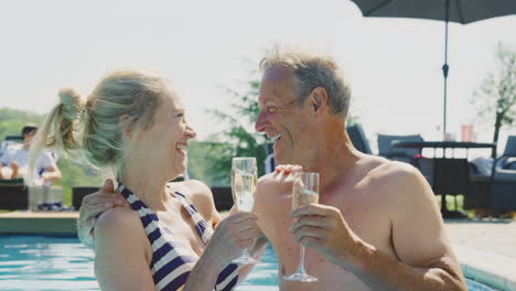 Retrato-De-Una-Pareja-Mayor-Relajándose-En-La-Piscina-Durante-Las-Vacaciones-De-Verano-Celebrando-Con-Champán