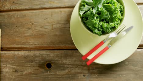 Lettuce-in-bowl-with-cutlery-placed-on-wooden-table-4K-4k