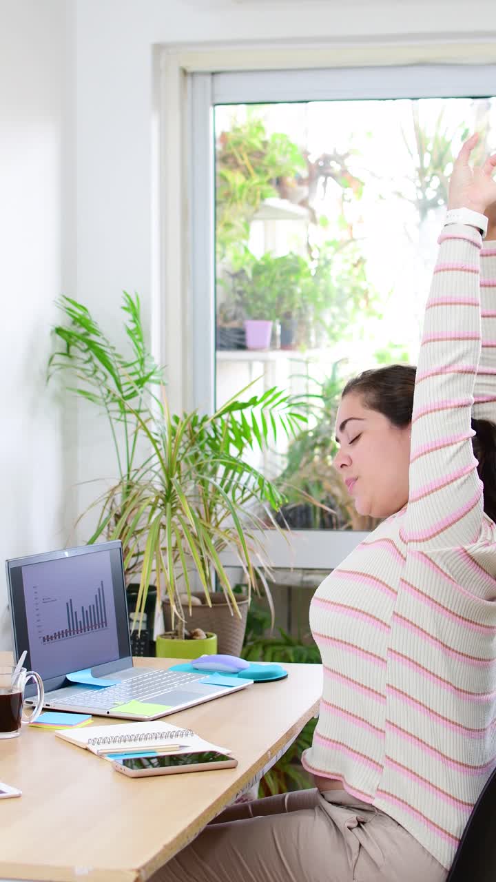 young lady during a break sitting by the table and stretching her arms from hard work