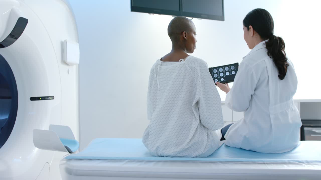 Due donne, una paziente in camice e una clinica seduta accanto allo scanner, mostrano scansioni su un tablet e spiegano i risultati.