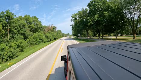 pov from vehicle roof - driving on a country road with a paved bike path; driving past homes and trees in late summer in the des moines river valley in central iowa; concepts of farming and rural life