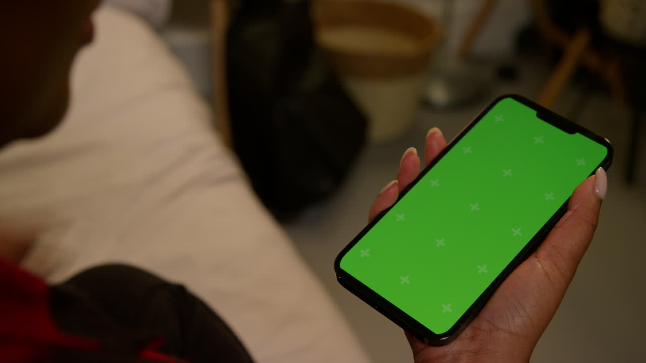 donna con un telefono con uno schermo verde in una camera da letto