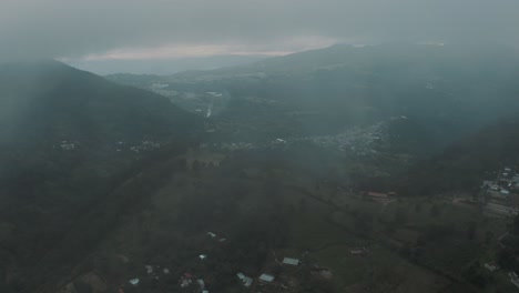 Drone-aerial-flying-through-clouds-revealing-green-valley-surrounded-by-mountains-in-Guatemala