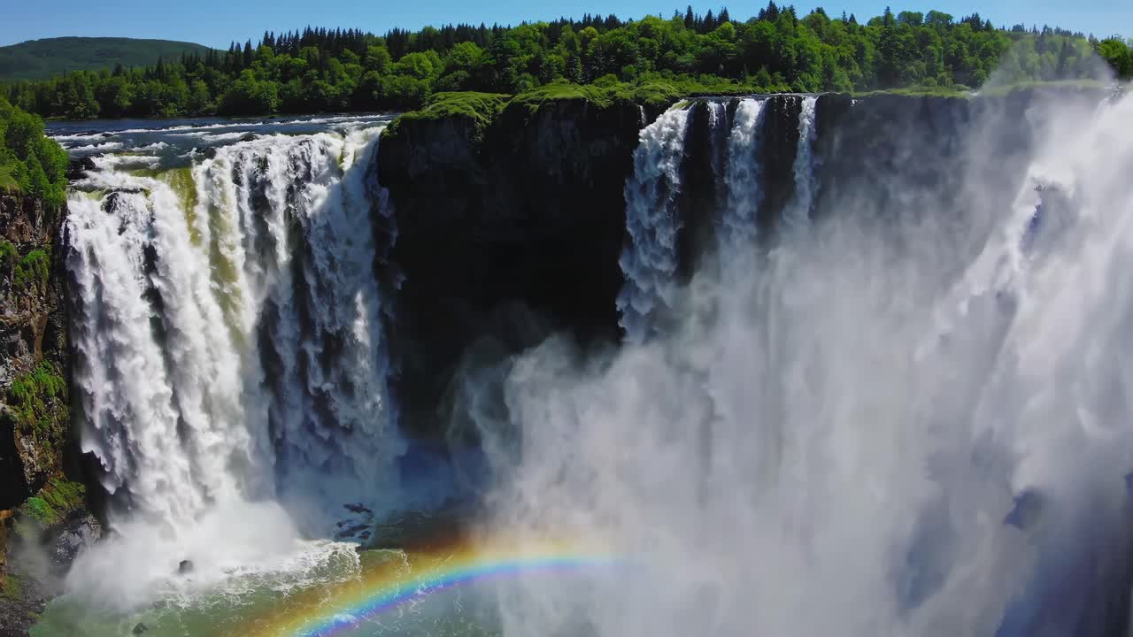 Aerial video captures a majestic waterfall cascading into a misty gorge, with a vibrant rainbow