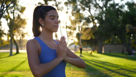 A-beautiful-young-hispanic-woman-looking-calm-and-relaxed-in-a-prayer-yoga-pose-during-a-meditation-class-in-the-park-at-sunrise