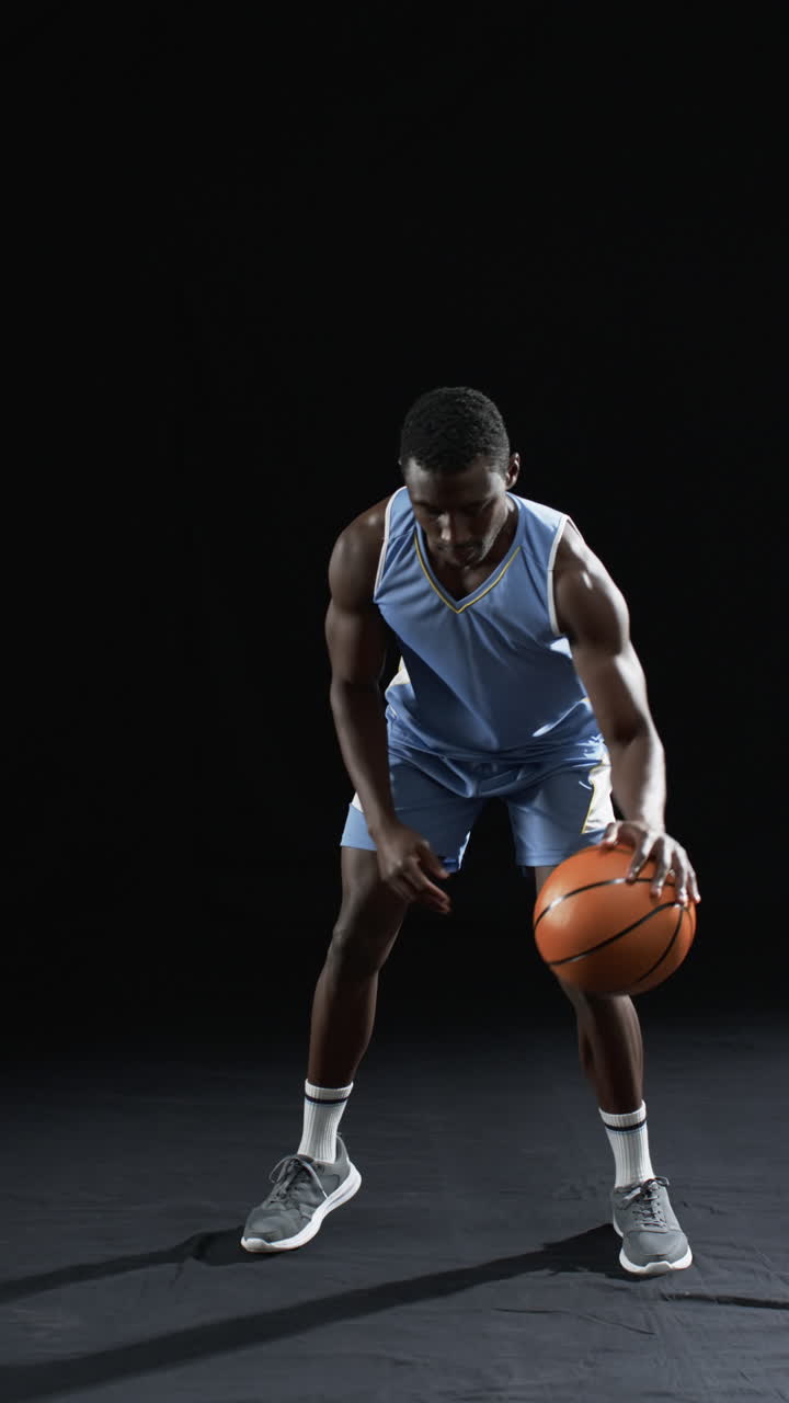 Vertical video: African American athlete bouncing basketball, black background