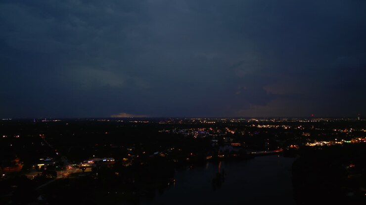 Le luci della città brillano sotto un cielo crepuscolare scuro, i fulmini rimbalzano e illuminano di bianco e giallo
