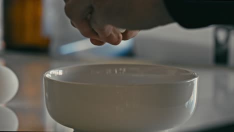 hands opening raw egg into a white bowl to make breakfast