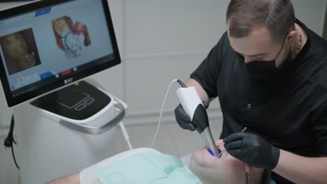 doctor scans the patient's teeth in the clinic. the dentist holds in his hand a manual 3d scanner for the jaw and mouth. dental health. creates a 3d model of teeth and gums on a medical monitor.