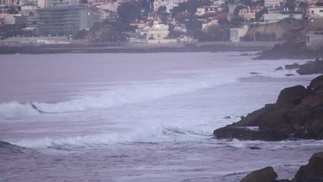 Vista-Aérea-De-Algunas-Pequeñas-Olas-Ordenadas-Cascais-Portugal-Pequeña-Ciudad,-Pequeña-Carretera-Costera-Con-Coche-Conduciendo-A-Lo-Largo-Del-País-Cerca-De-La-Playa-Del-Acantilado-Rocoso-Del-Océano