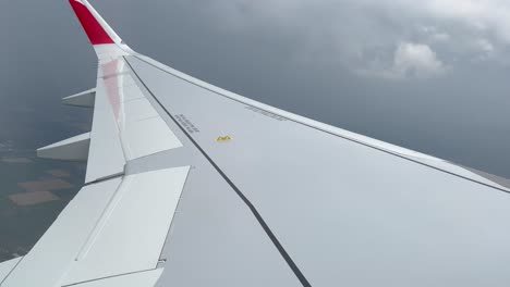 Left-wing-view-of-a-jet-plane-while-crossing-a-thunderstorm-with-rain,-daylight