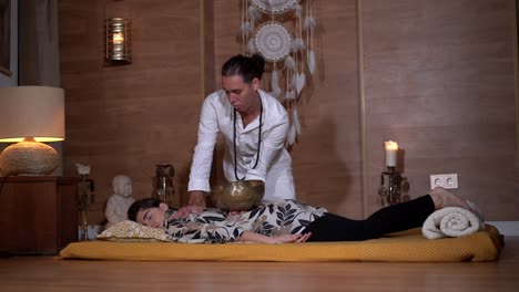 Zen-master-playing-bowl-gong-above-relaxed-woman-during-meditation