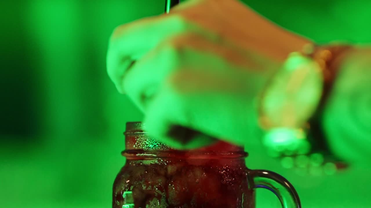 Hand inserting a straw into a red cocktail with a slice of lemon