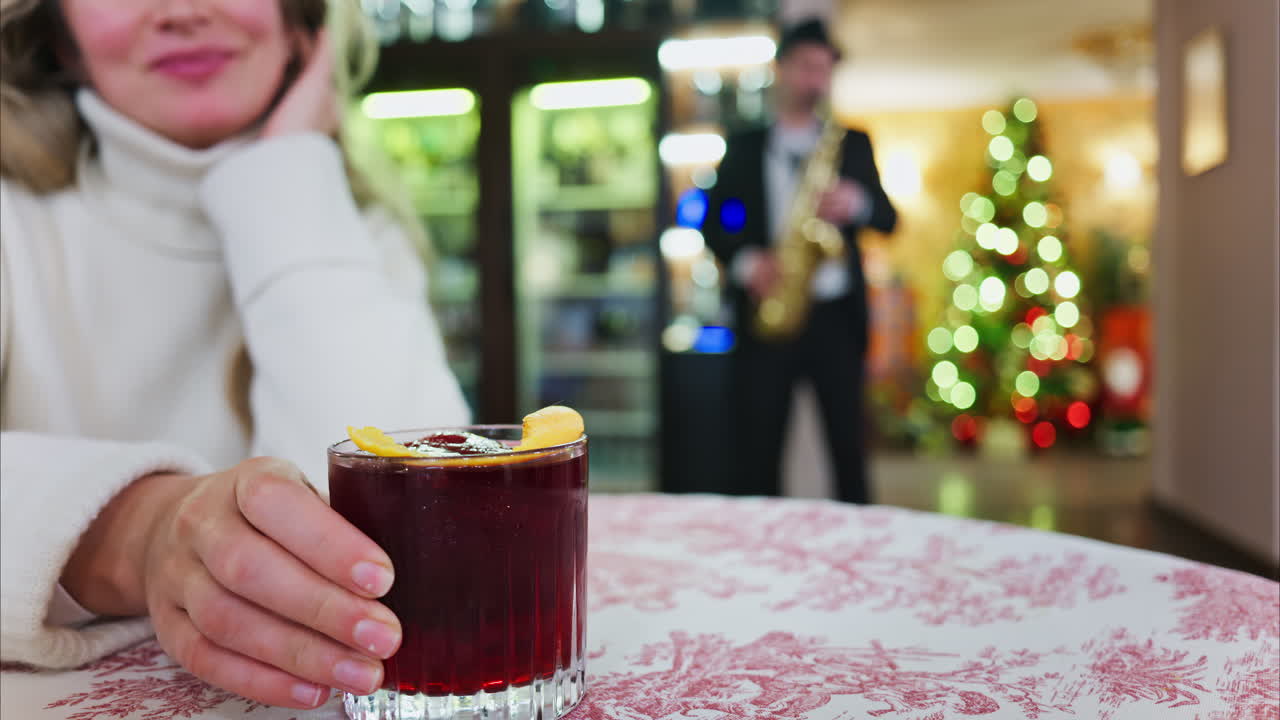 Nahaufnahme einer Frau mit einem Negroni-Cocktail auf einer rot-weißen Tischdecke in einem Restaurant mit einem Weihnachtsbaum im Hintergrund