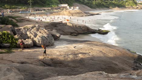 pan de lapso de tiempo de movimiento que muestra parte de la roca arpoador en ipanema y gente disfrutando de la playa de los diablos con la montaña de pan de azúcar y el fuerte de copacabana siguiendo la sombra en primer plano