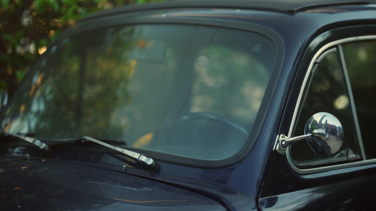 Primo piano del parabrezza e dello specchietto retrovisore cromato di un'auto d'epoca blu scuro.