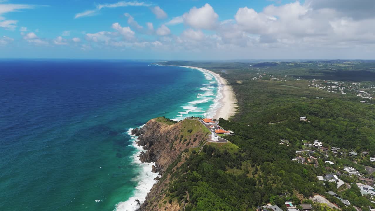 Aerial view of Cape Byron Lighthouse at Byron Bay during sunny day in Australia. Wide shot. Beautiful sandy beach and turquoise ocean waves.