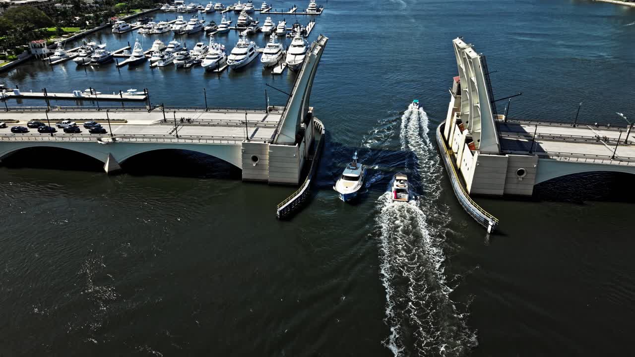 Aerial: two boats crossing under Royal Park Bridge during the day in West Palm Beach, Florida, USA, orbit drone shot