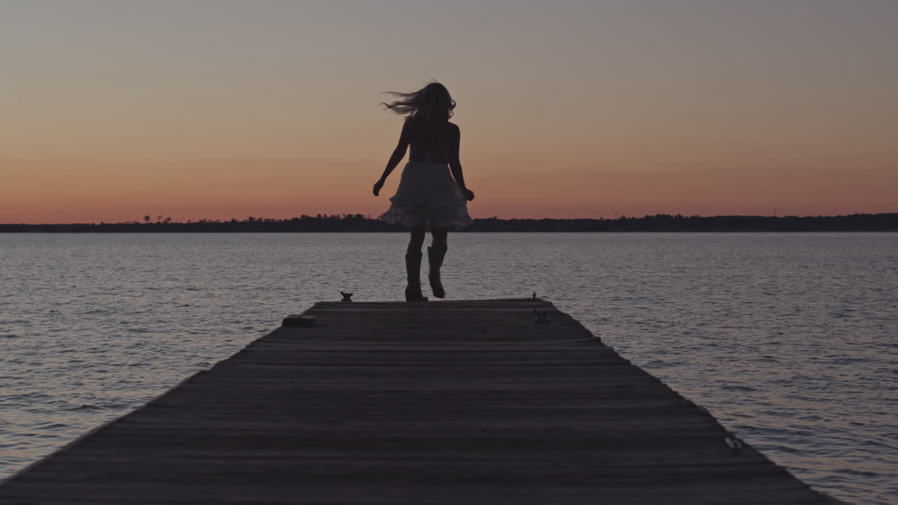 Bella ragazza che volteggia con un vestito su un molo al tramonto.