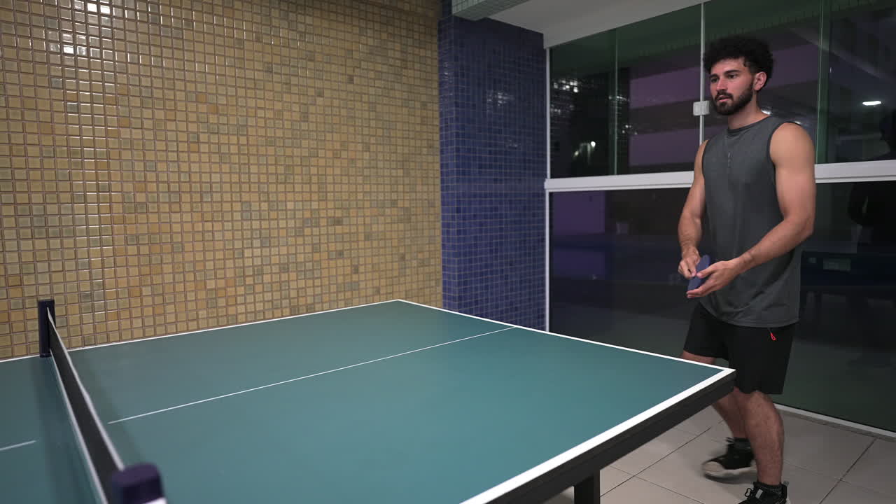 Joven latino practicando ping pong o tenis de mesa en interiores para mantenerse sano y llevar un estilo de vida activo