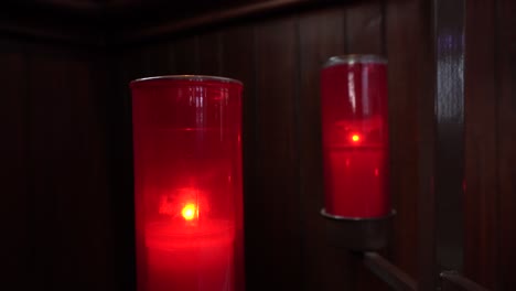 Zwei-Rote-Kerzen,-Die-In-Einer-Kirche-Hinter-Einer-Holzwand-Brennen