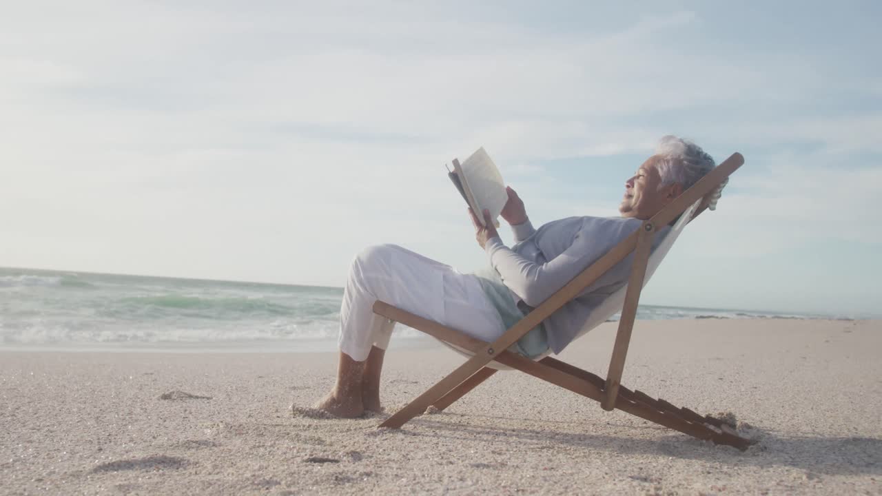 Latin senior hispanic woman relaxing on sunbed on beach at sunset, reading book