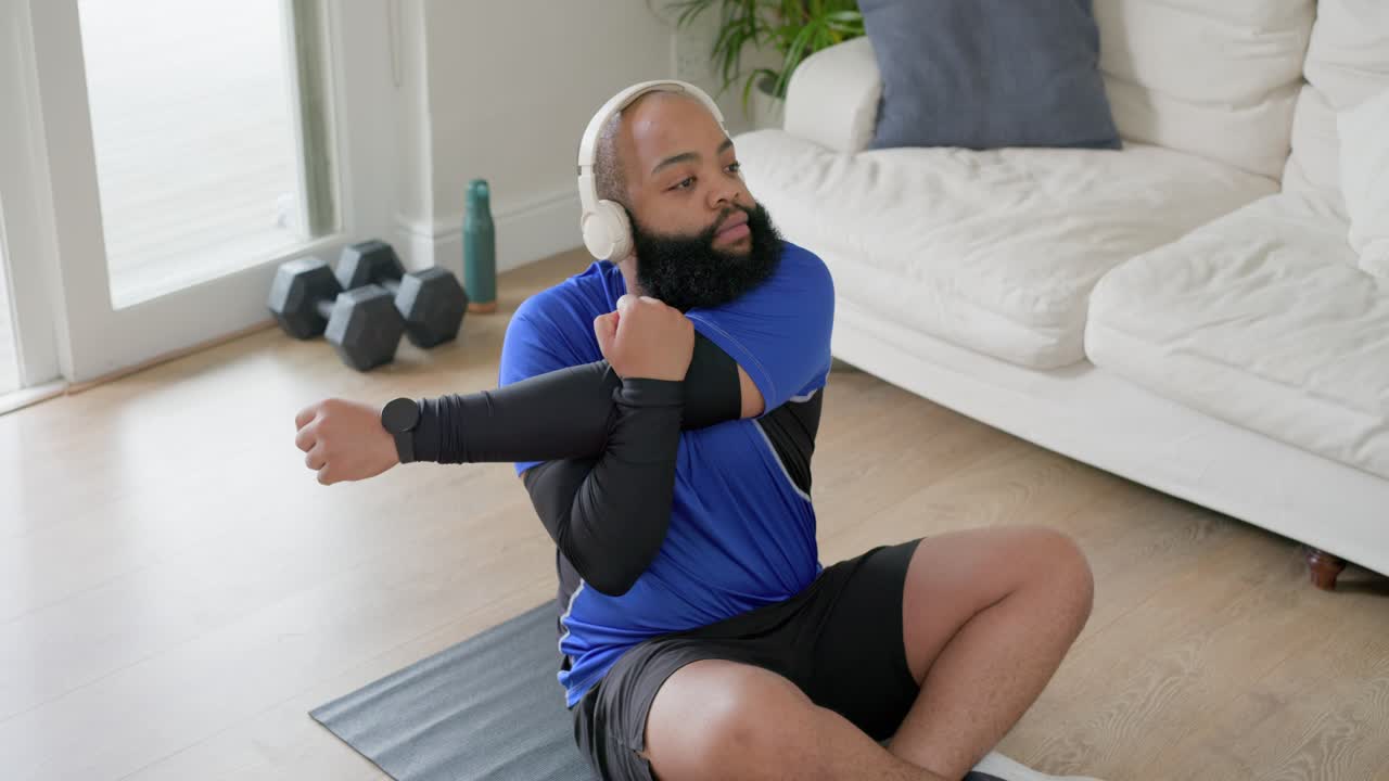 African American man checking smartwatch then stretching shoulders on dark mat at home warming up