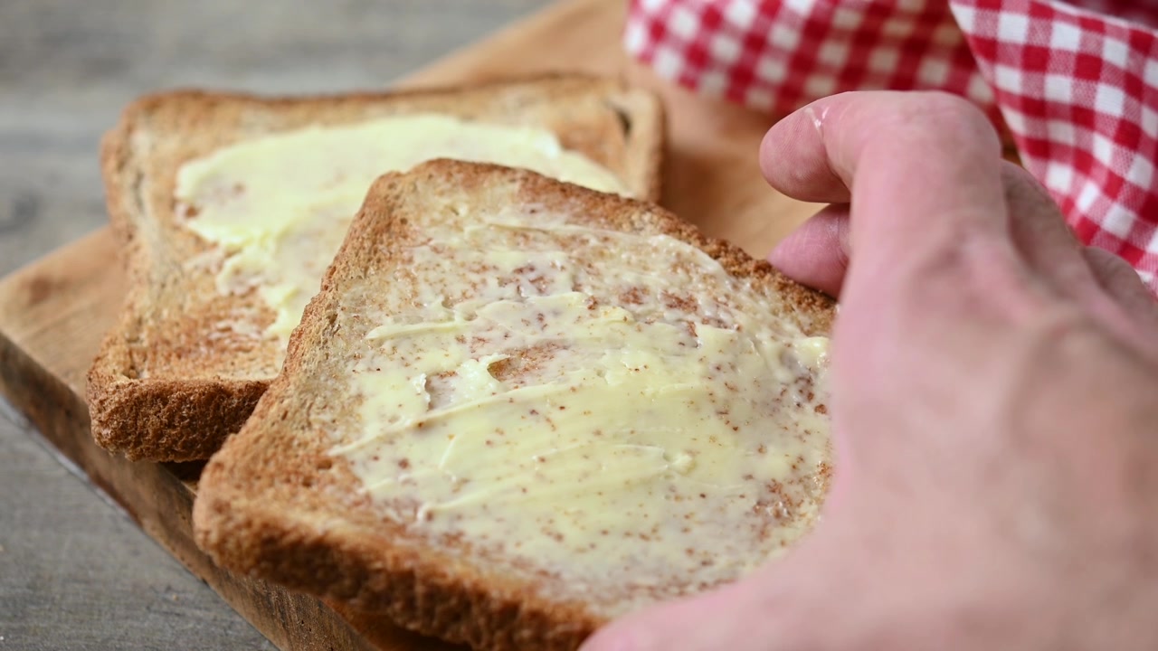 Mano che posiziona toast imburrato su un tagliere di legno