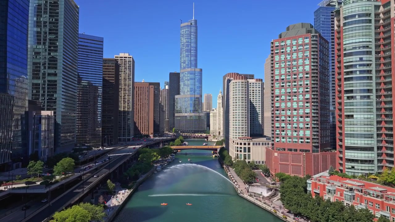 Vista aérea de drone em ângulo elevado acompanhando o Rio Chicago fluindo pelo centro da cidade, cercado por arranha-céus modernos de vidro em um dia claro de verão